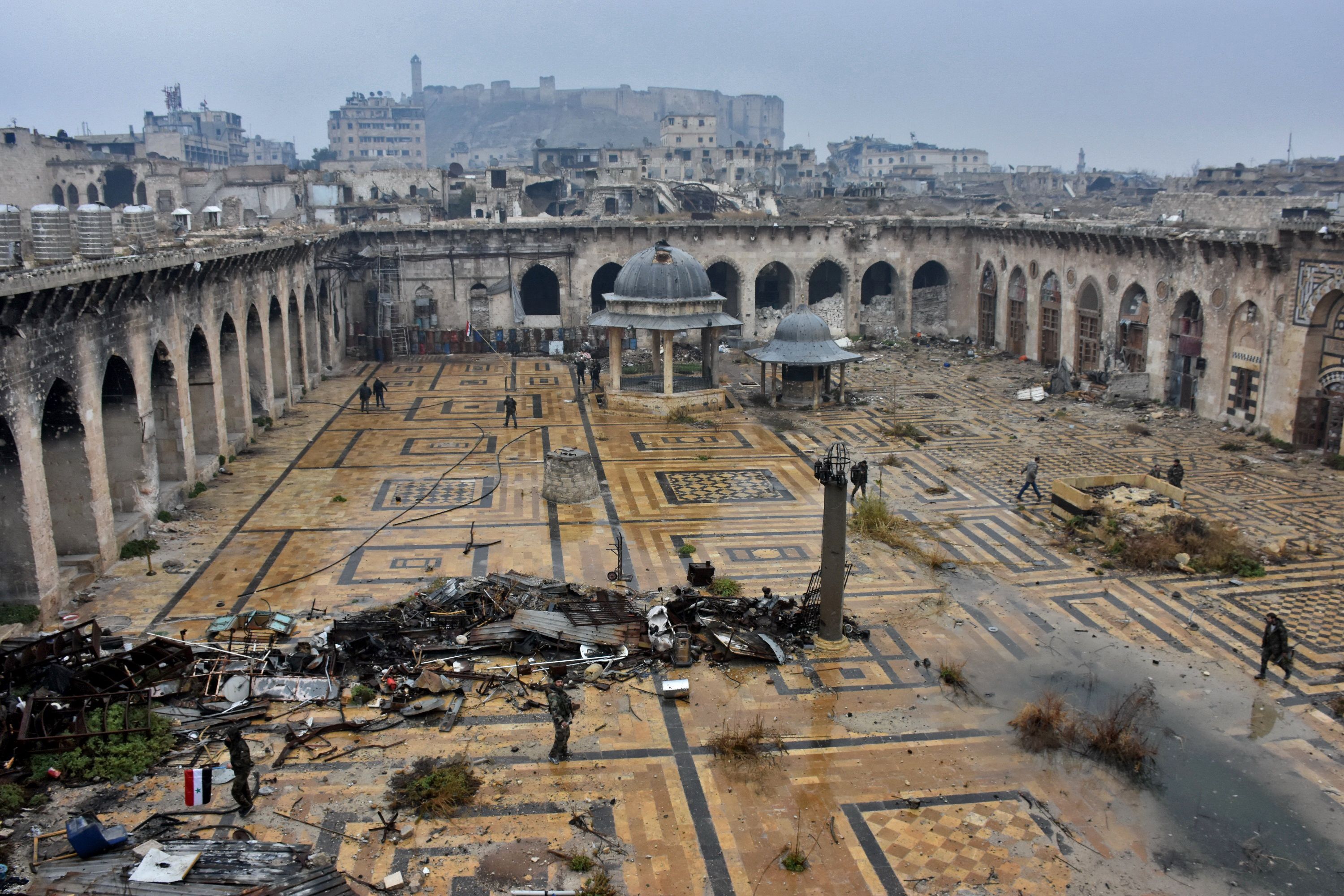 A general view shows Syrian pro-government forces walking in the ancient Umayyad mosque in the old city of Aleppo in the foreground and the city's citadel in the background on December 13, 2016, after they captured the area. After weeks of heavy fighting, regime forces were poised to take full control of Aleppo, dealing the biggest blow to Syria's rebellion in more than five years of civil war.  / AFP / George OURFALIAN