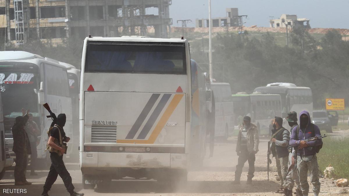 Rebel fighters stand guard as a convoy of buses (R) carrying Sunni rebels and civilians, who were evacuated from Zabadani and Madaya, as part of a reciprocal evacuation deal for four besieged towns, travel in al-Rashideen to journey towards rebel-held Idlib, Syria April 21 2017. REUTERS/Ammar Abdullah