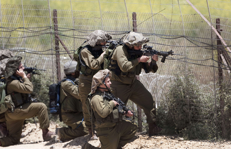 Israeli soldiers keep their position along Israel’s border with Syria as demonstrators trying to head into the Israeli-annexed Golan Heights gather on the other side of the fence, as seen from the Druze village of Majdal Shams, on June 5, 2011 as Israeli troops opened fire at protestors from Syria who stormed a ceasefire line in the occupied Golan Heights, killing three demonstrators, according to Syrian television. AFP PHOTO/MENAHEM KAHANA