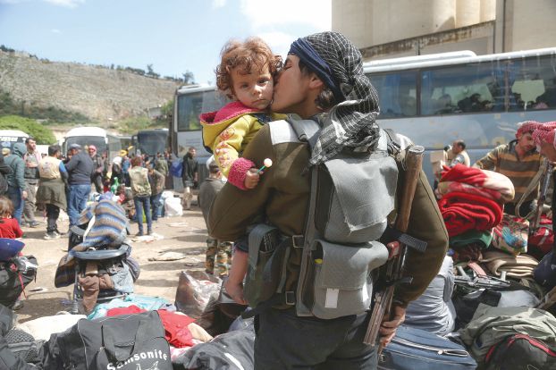 TOPSHOT - A rebel fighter from Eastern Ghouta, holds his weapon as he kisses a child after arriving in Qalaat al-Madiq, some 45 kilometres northwest of the central city of Hama, on March 30, 2018, following the ongoing evacuation deals made between rebel fighters and Russia, an ally of the Syrian President. / AFP PHOTO / Zein Al RIFAI