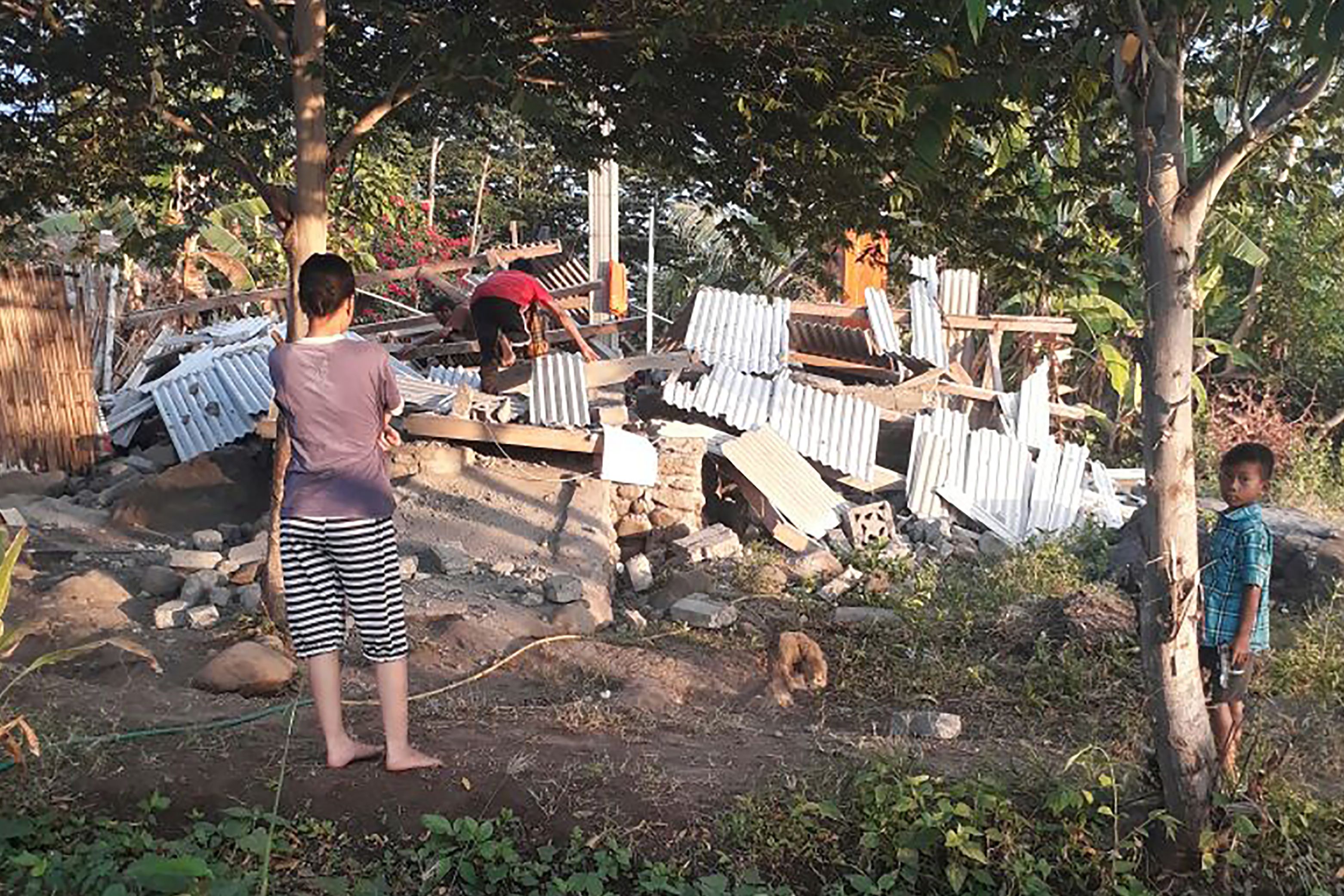 This handout photograph taken on July 29, 2018 and released by the Nusa Tenggara Barat Disaster Mitigation Agency (BPBD) show an Indonesian person (C) scrambling over the collapsed ruins of a house as others look on following an earthquake in Lombok.
A shallow 6.4-magnitude quake struck the Indonesian island of Lombok on July 29, the United States Geological Survey said. / AFP PHOTO / Nusa Tenggara Barat Disaster Mitigation Agency / Handout / RESTRICTED TO EDITORIAL USE - MANDATORY CREDIT "AFP PHOTO / Nusa Tenggara Barat Disaster Mitigation Agency" - NO MARKETING NO ADVERTISING CAMPAIGNS - DISTRIBUTED AS A SERVICE TO CLIENTS