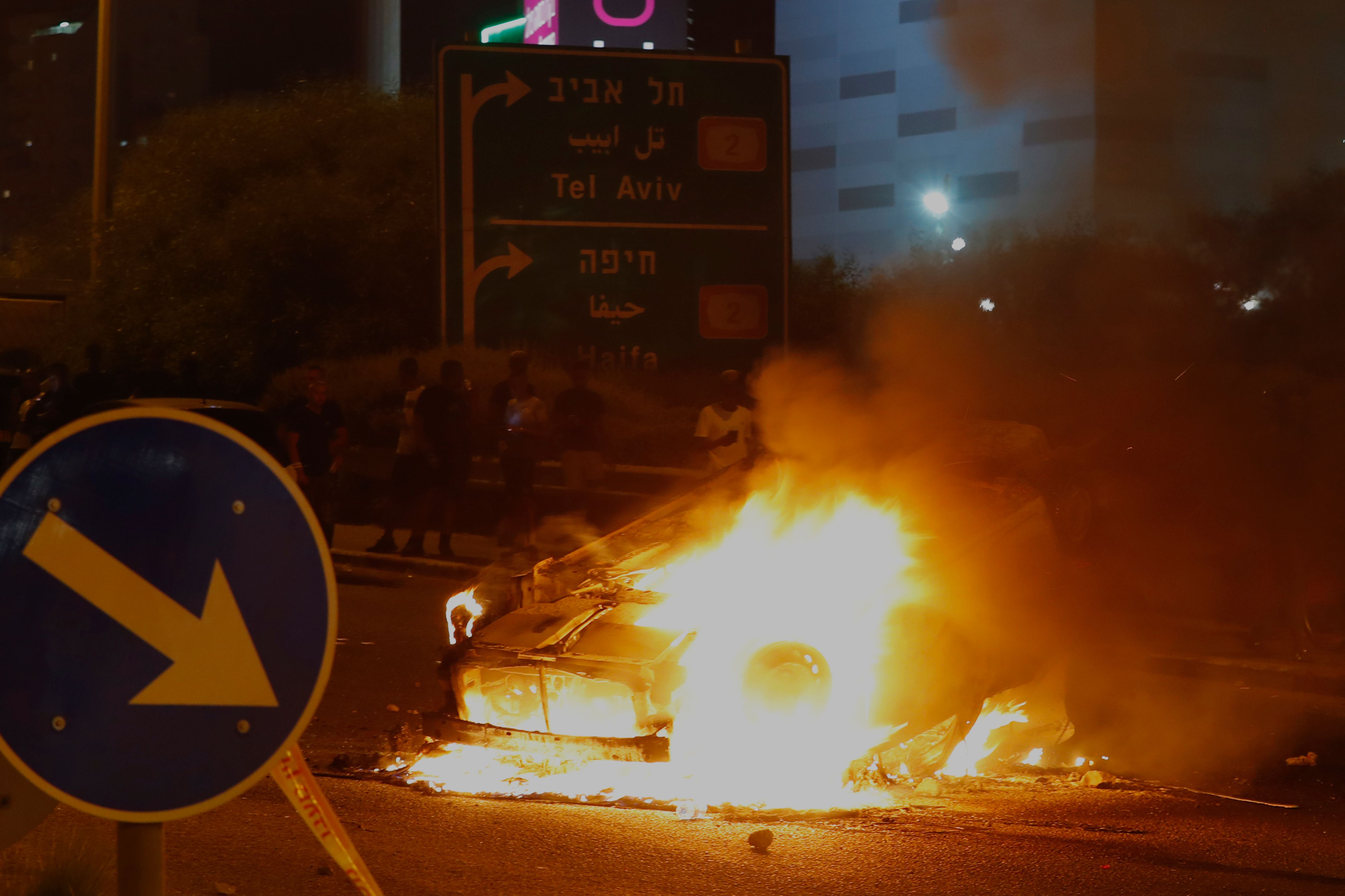 A burning and overturned police car blocks an entrance to the Israeli coastal city of Netanya on July 2, 2019, during a protest against the killing of Solomon Tekah, a young man of Ethiopian origin, who was killed by an off-duty police officer. Angry protesters clashed with Israeli police on July 2 over an off-duty officer's killing of a young man of Ethiopian origin, as the incident drew fresh accusations of racism. Crowds of Ethiopian Israelis battled police and blocked highways on at least 15 junctions across the country, with 47 officers wounded and 60 demonstrators detained, according to a police statement. Solomon Teka, reportedly 18 or 19, was buried on July 2, after he was shot dead in Kiryat Haim, a town near the northern port city of Haifa, late Sunday. / AFP / JACK GUEZ