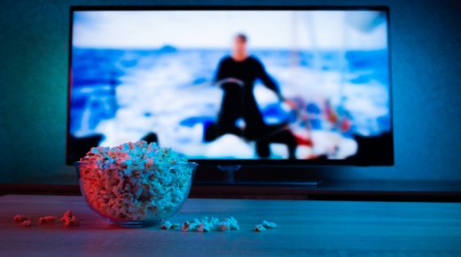 Popcorn in a glass plate on the background of the TV. Color bright lighting, blue and red. Background