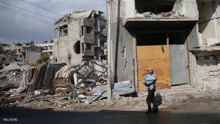 A man carries a baby near damaged buildings in the rebel held besieged city of Douma, in the eastern Damascus suburb of Ghouta, Syria December 30, 2016. REUTERS/Bassam Khabieh