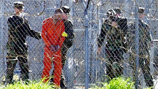 Guantanamo Bay, CUBA: FOR USE WITH AFP STORIES: US-attacks-UN-Guantanamo (FILES) This 17 January, 2002, file photo shows a detainee (2nd L) wearing an orange jump suit surrounded by heavy security at the US Guantanamo Naval Base in Cuba. UN experts said on 16 February, 2006, the US must shut down the detention center without delay and release or try its inmates. The demand came in a report by five independent experts who act as monitors for the UN Human Rights Commission. The document charged that US treatment of the more than 500 "war on terror" detainees held in legal limbo at the naval base in Cuba violated their rights to physical and mental health and in some cases amounted to torture. The White House blasted the UN report, alleging abuse of inmates and calling for closing the facility, as "a discredit to the UN." AFP PHOTO/ROBERTO SCHMIDT/FILES (Photo credit should read ROBERTO SCHMIDT/AFP/Getty Images)